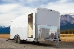 Front three-quarter view of a Royal Cargo enclosed trailer with a side entry door and diamond-plate front paneling in a scenic mountain setting.