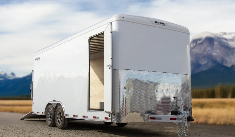 Front three-quarter view of a Royal Cargo enclosed trailer with a side entry door and diamond-plate front paneling in a scenic mountain setting.