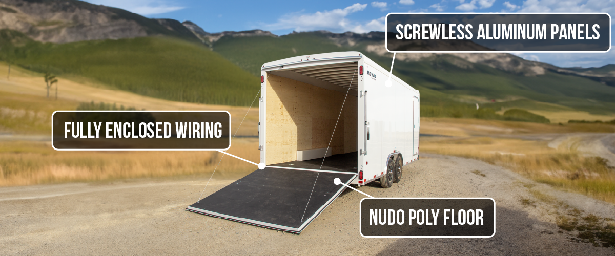Rear-angle view of a Royal Cargo enclosed trailer with the ramp door open, featuring on-image callouts highlighting fully enclosed wiring, screwless aluminum panels, and a Nudo poly floor, set in a mountain landscape.