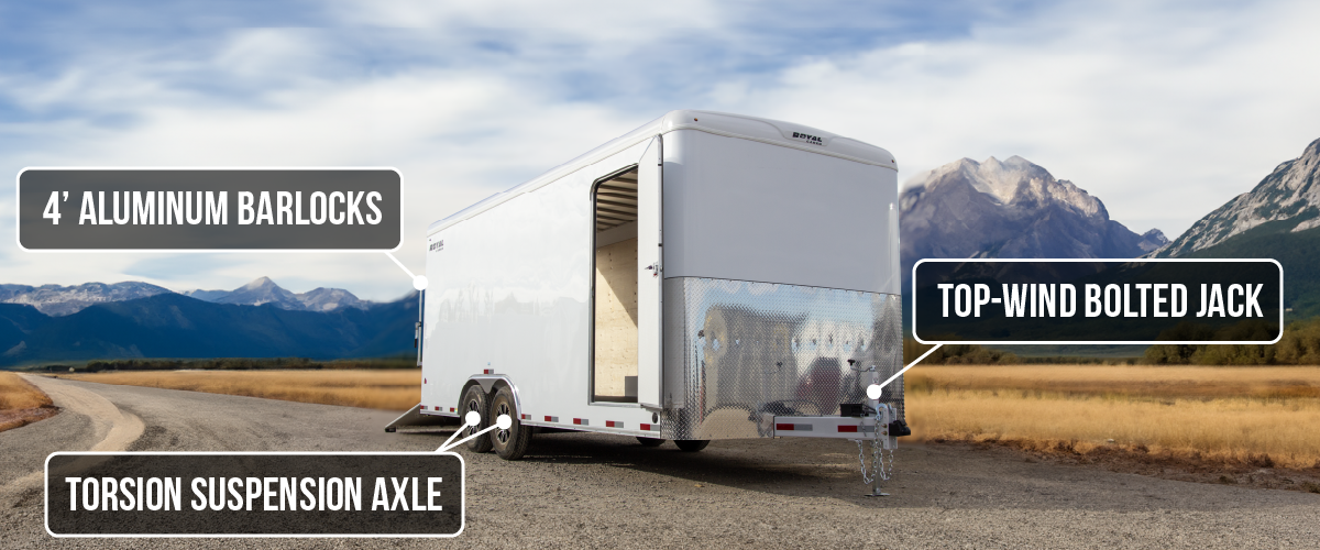 Front-side view of a Royal Cargo enclosed trailer with on-image labels pointing out the 4-foot aluminum barlocks, torsion suspension axle, and top-wind bolted jack, with mountains in the background.